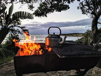 A braai fire and kettle with the sea in the background at dusk